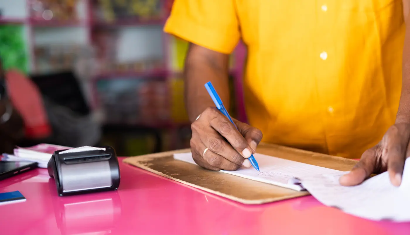 Un commerciante scrive un ordine a penna su un blocco, accanto al registratore di cassa